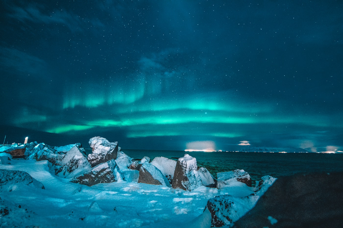 Green aurora over snow-covered rocks on a dark Icelandic shore at night
