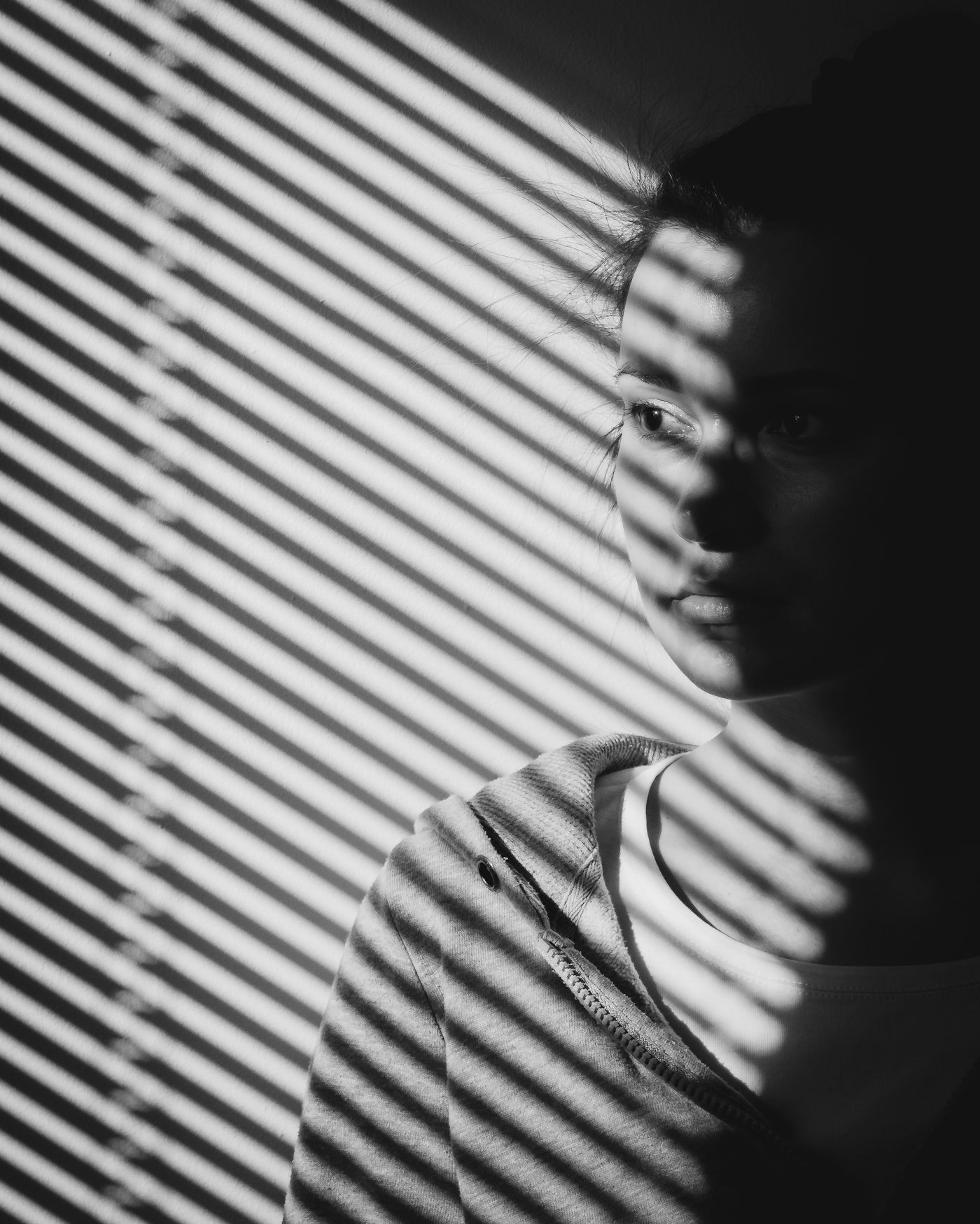 Portrait half-lit through window blinds, bands of light falling across the face and wall