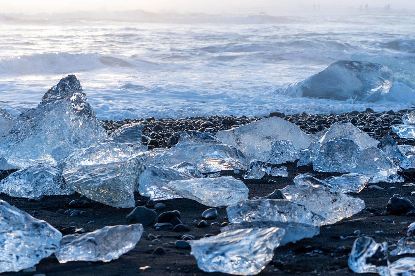 Blocks of glacier ice stranded on black volcanic sand as surf breaks behind them