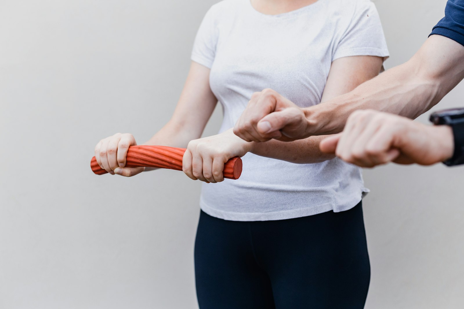 Close view of a therapist's hands supporting a patient's forearm as she grips a red foam bar for wrist strengthening.