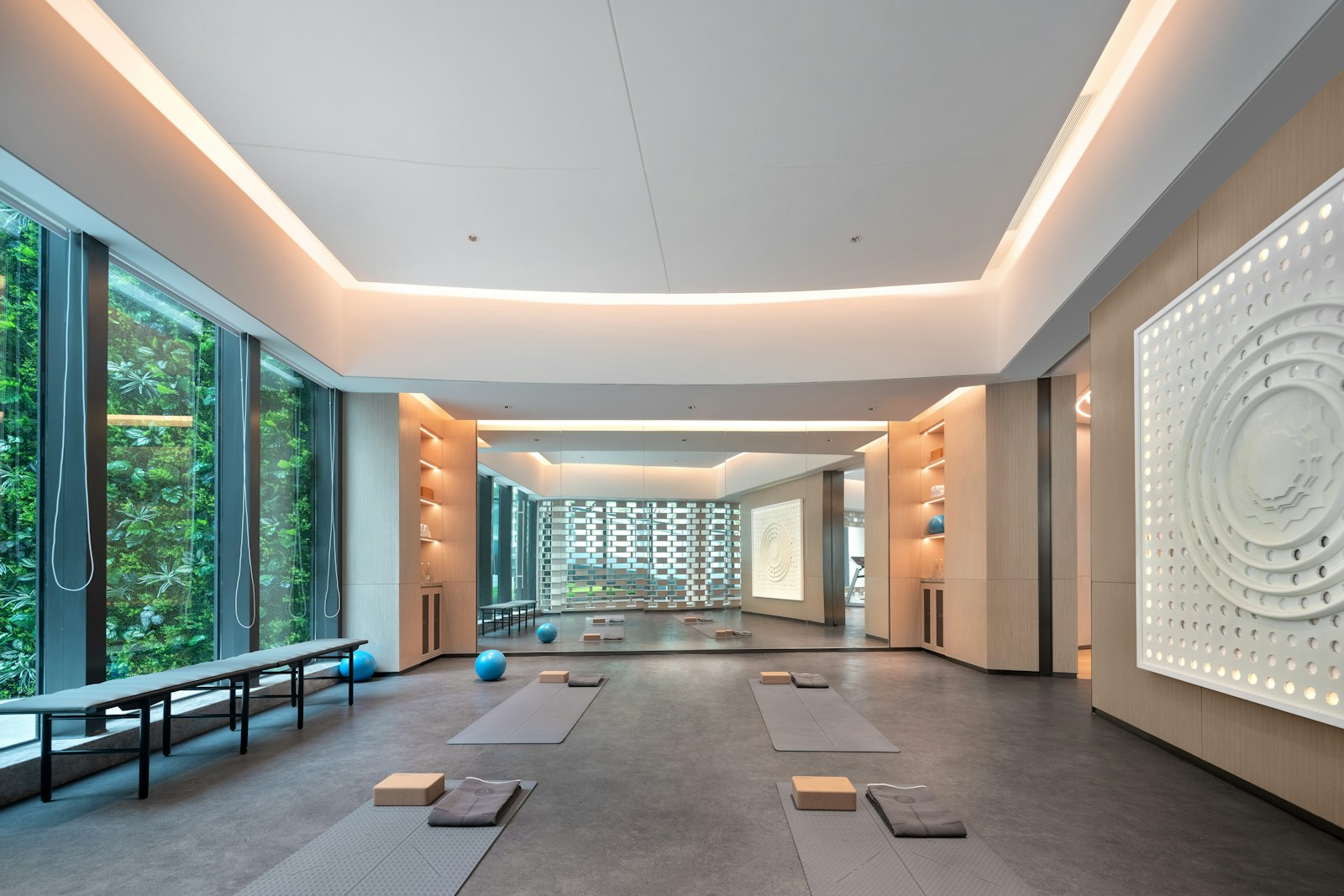 An open, daylit movement studio with mats, blocks and folded towels laid out on a grey floor.
