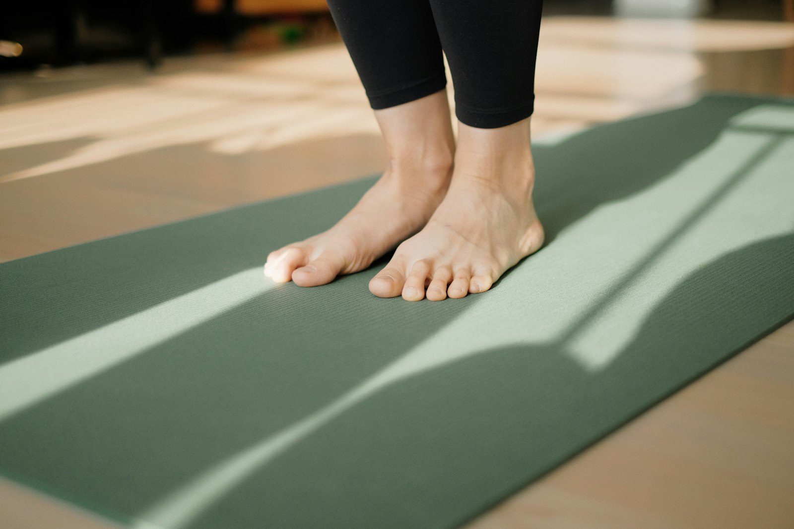 Bare feet standing on a sage green exercise mat in low window light