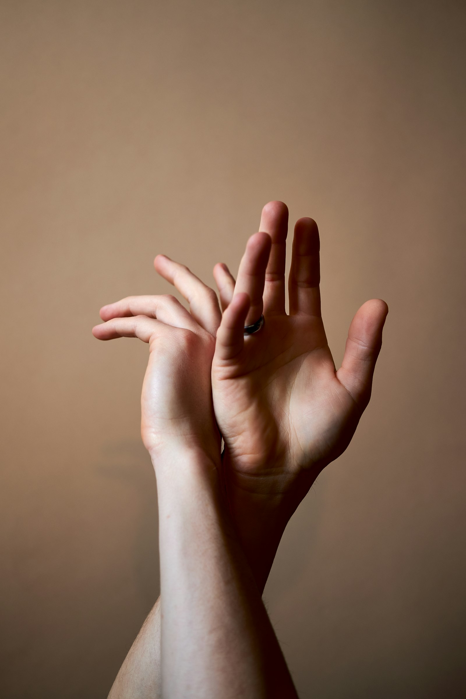 Two hands stretching against a warm plaster wall, fingers interlaced