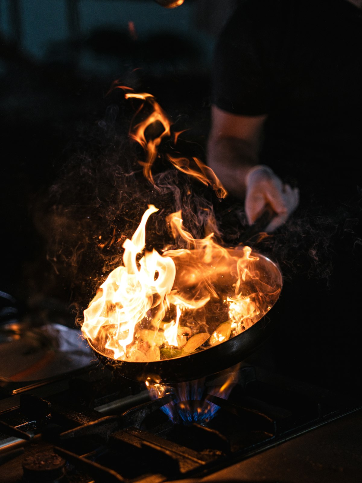 Flames rising from a pan at the open hearth in the dark Ember and Oak kitchen