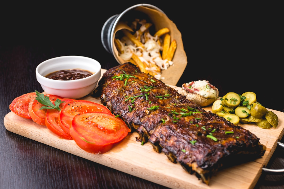 Oak-smoked ribs resting on a carving board with pickles and tomato