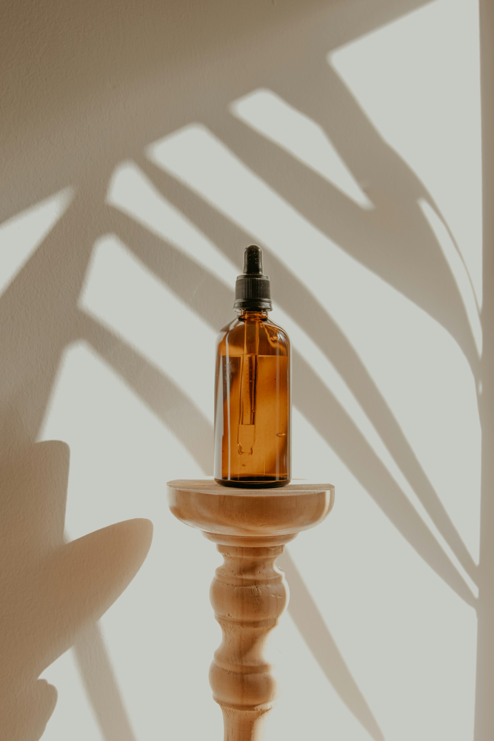 Amber glass dropper bottle of Meadowfoam Dew Serum on a wooden pedestal