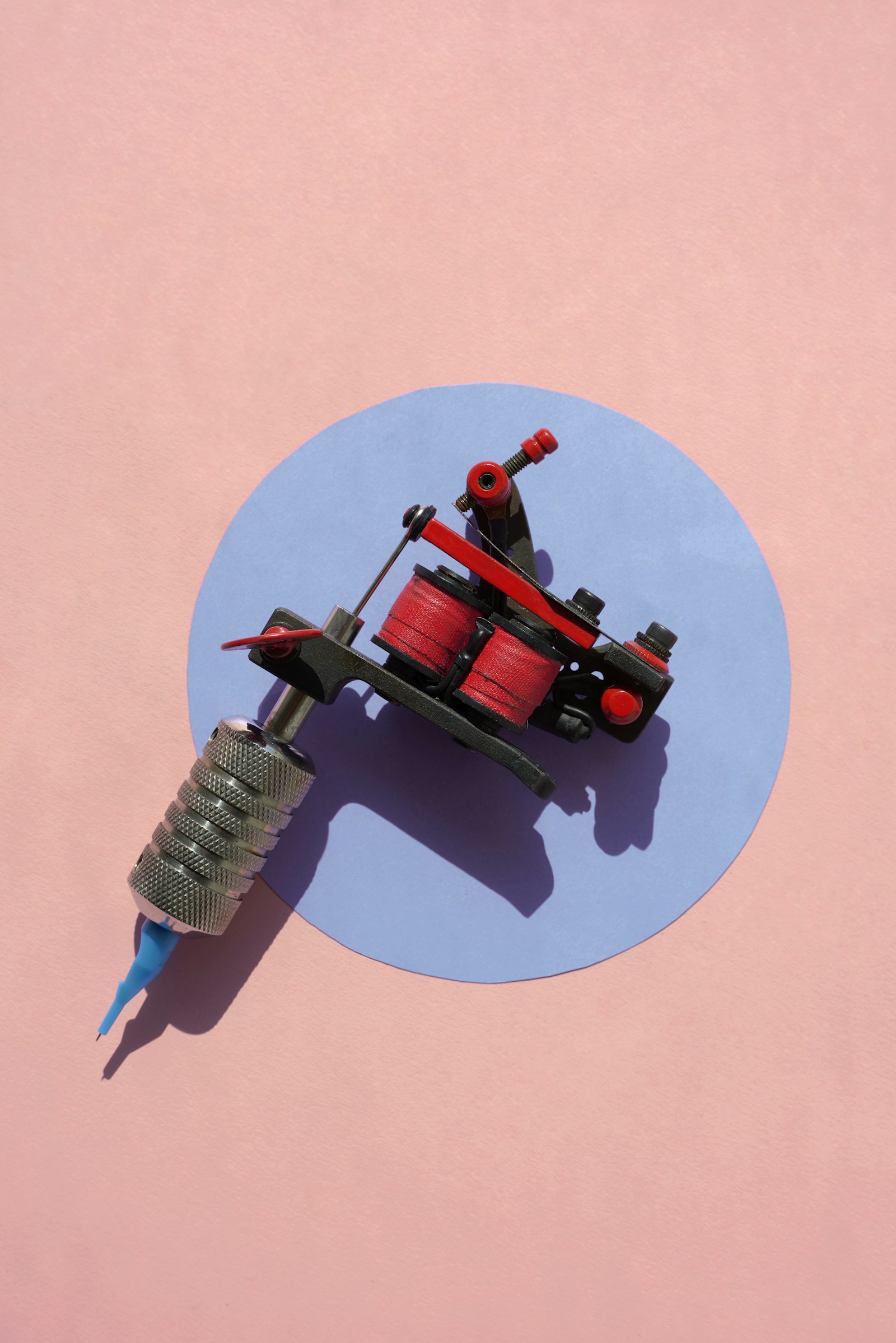 A coil tattoo machine photographed alone from above against a plain paper backdrop