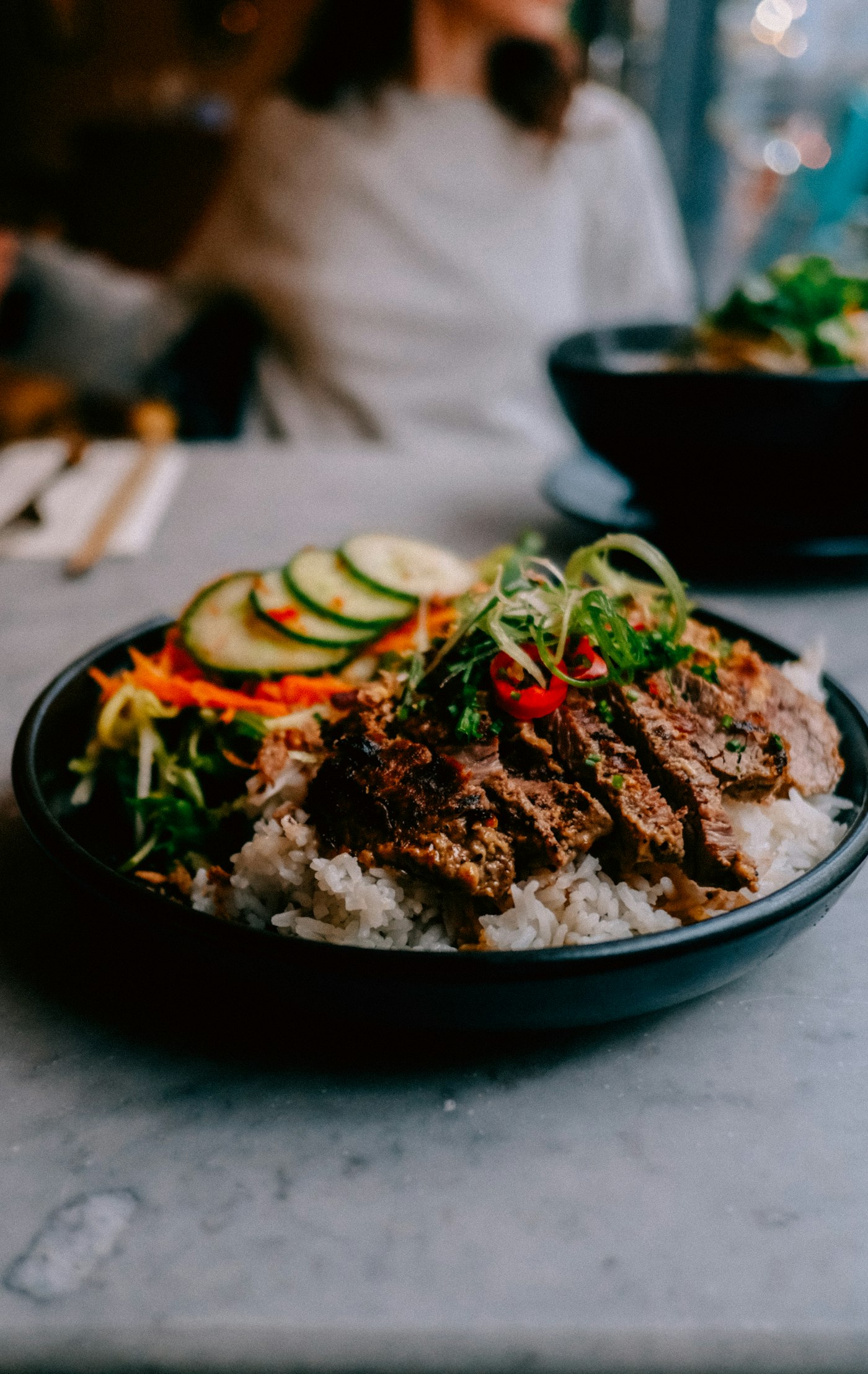 Tô cơm thịt bò nướng thái lát với dưa leo, cà rốt bào và rau thơm, rắc ớt đỏ