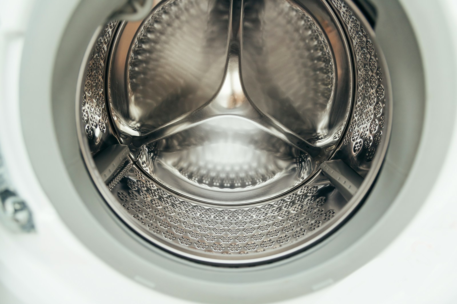 Cận cảnh lồng giặt inox sáng bóng nhìn xuyên qua cửa tròn máy giặt cửa ngang, các lỗ thoát nước dập đều.