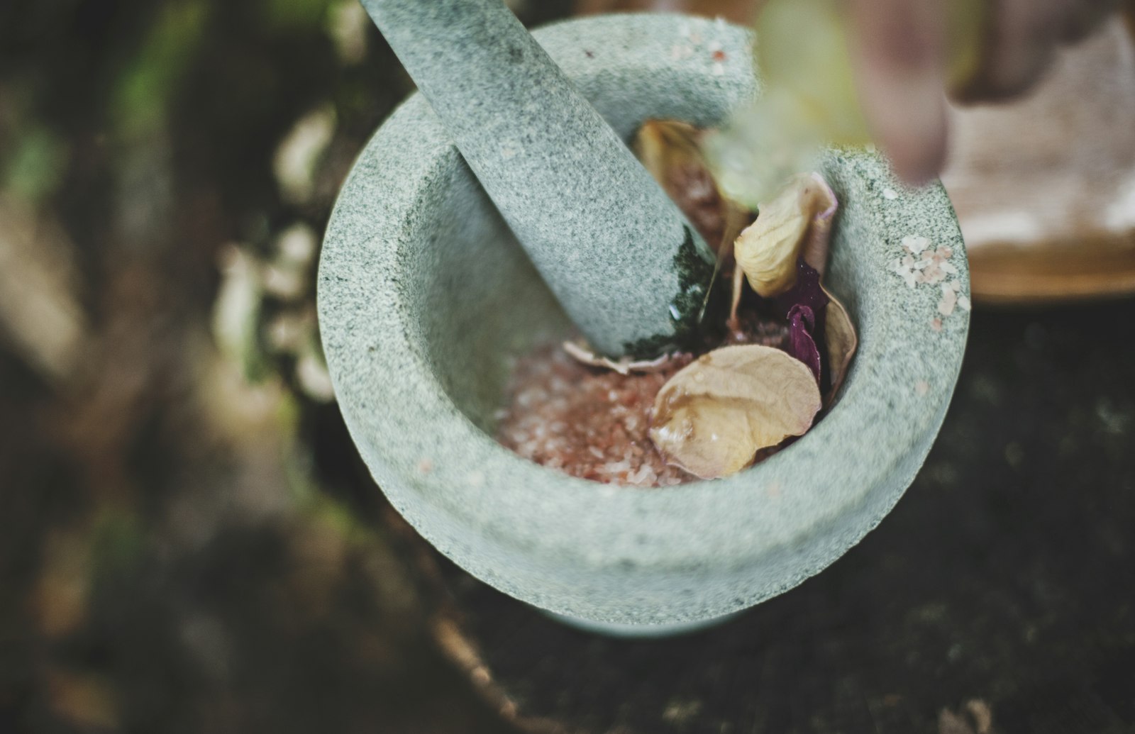 Cối và chày đá granit nhìn từ trên xuống, bên trong có muối hồng và cánh hoa khô đang được giã