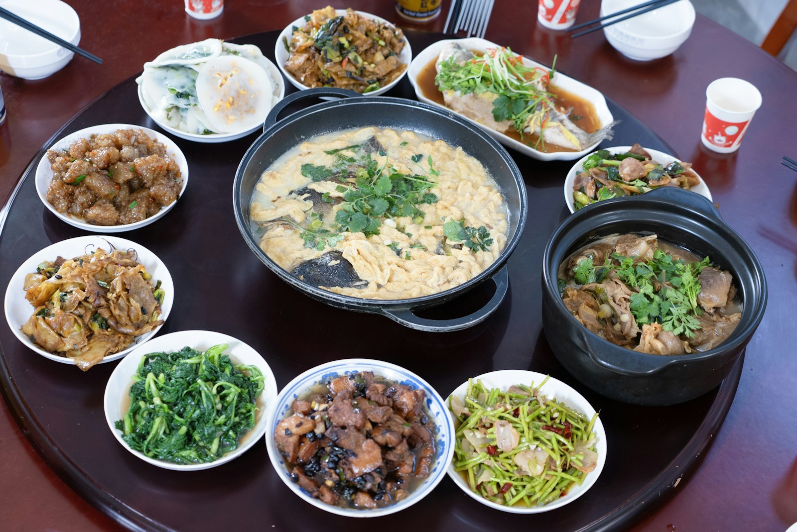Mâm tròn nhiều món Việt gồm cá hấp, thịt kho, rau luộc và canh bày kín mặt bàn.