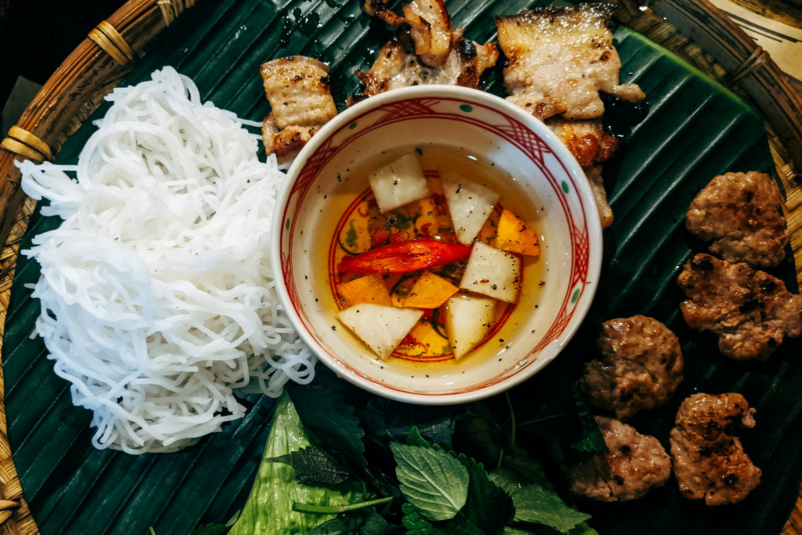 Bún tươi, thịt nướng và chả viên bày trên lá chuối cùng chén nước mắm chua ngọt.