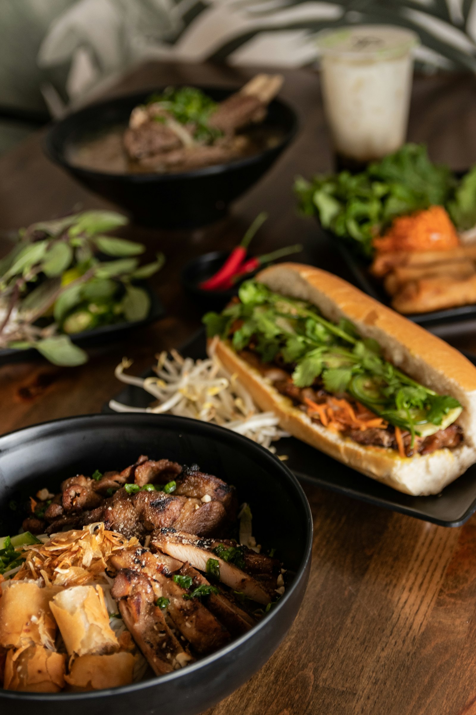 Tô bún thịt nướng với chả giò cắt khúc, bên cạnh là bánh mì kẹp thịt và rau thơm.
