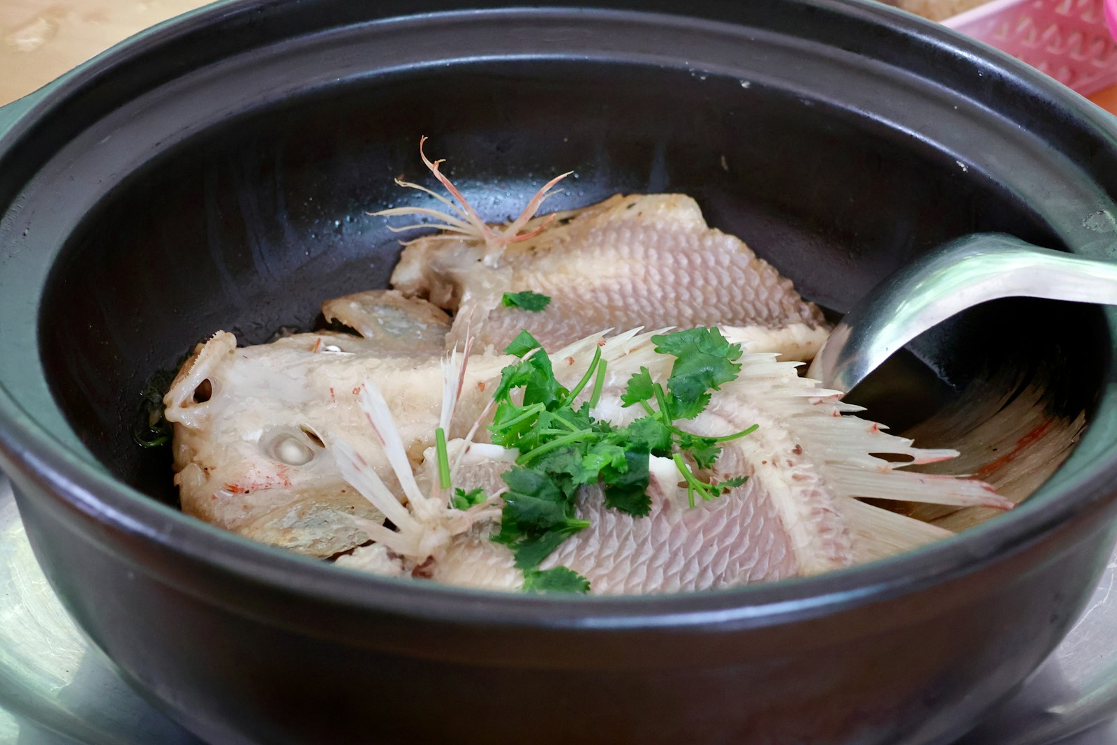 Cá hấp nguyên con trong nồi đất, rắc ngò rí và hành lá.