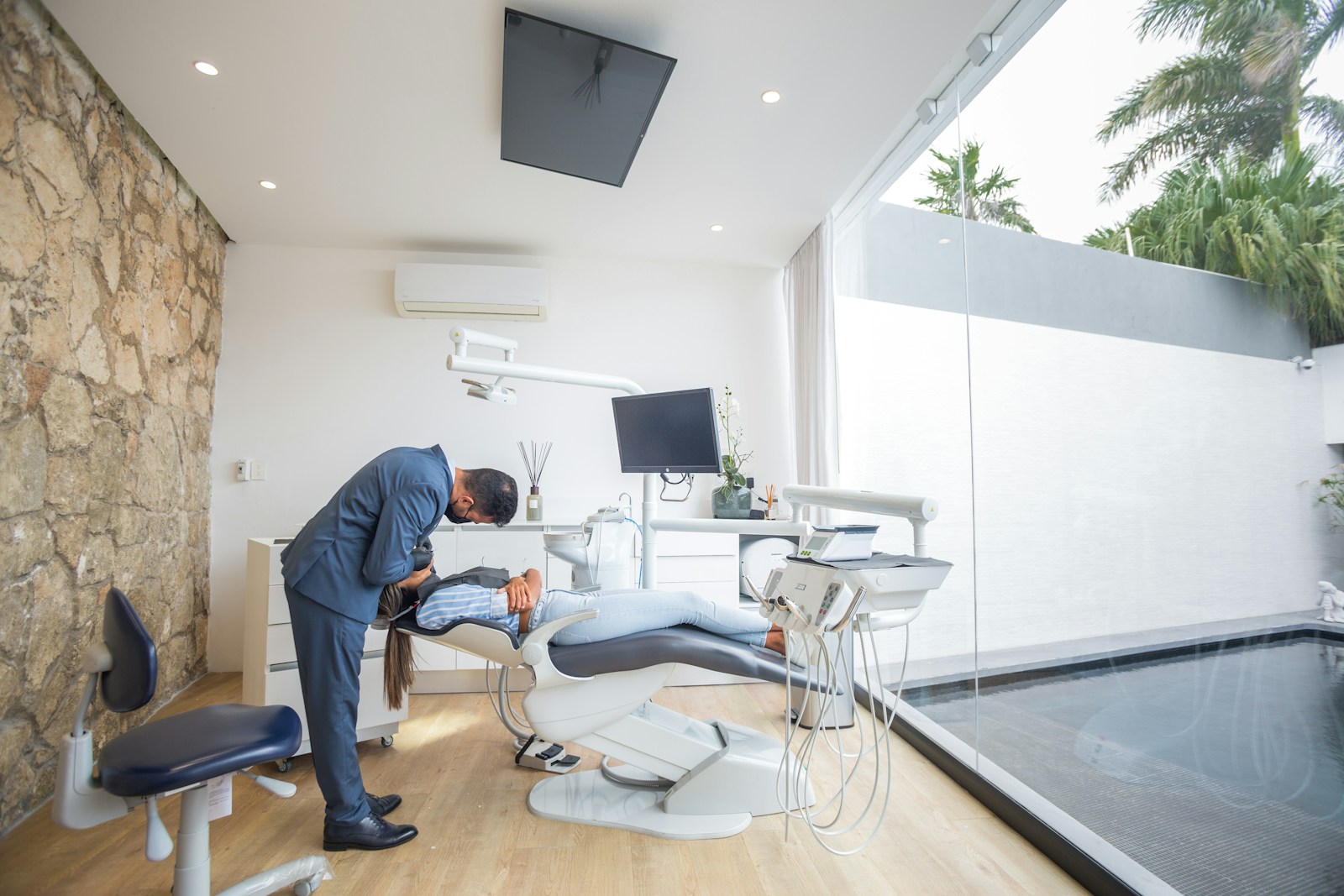 Phòng điều trị sáng có một bức tường đá tự nhiên, sàn gỗ và vách kính lớn nhìn ra hồ nước cùng hàng cây cọ