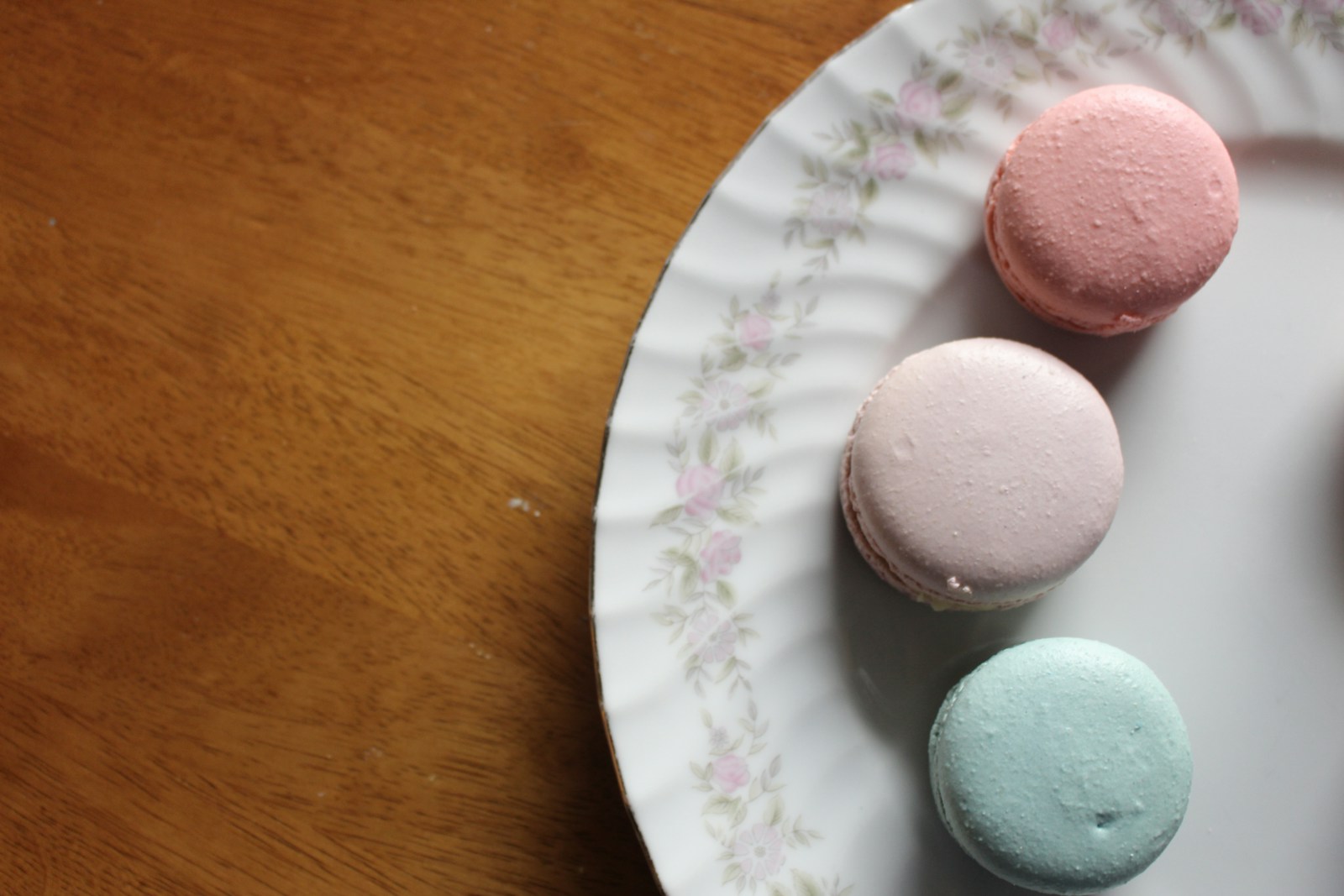 Ba chiếc bánh macaron hồng và xanh bạc hà trên đĩa sứ hoa nhỏ