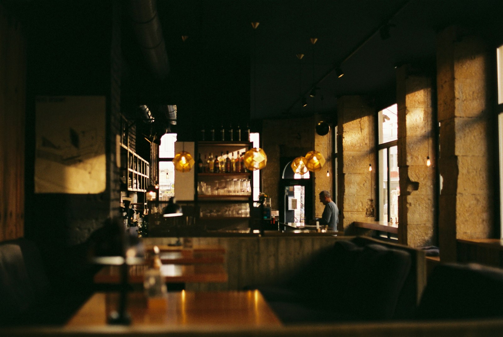 Bên trong quán về chiều: đèn thả thủy tinh vàng, cột đá, dãy ghế sofa và bàn gỗ, quầy bar phía sau