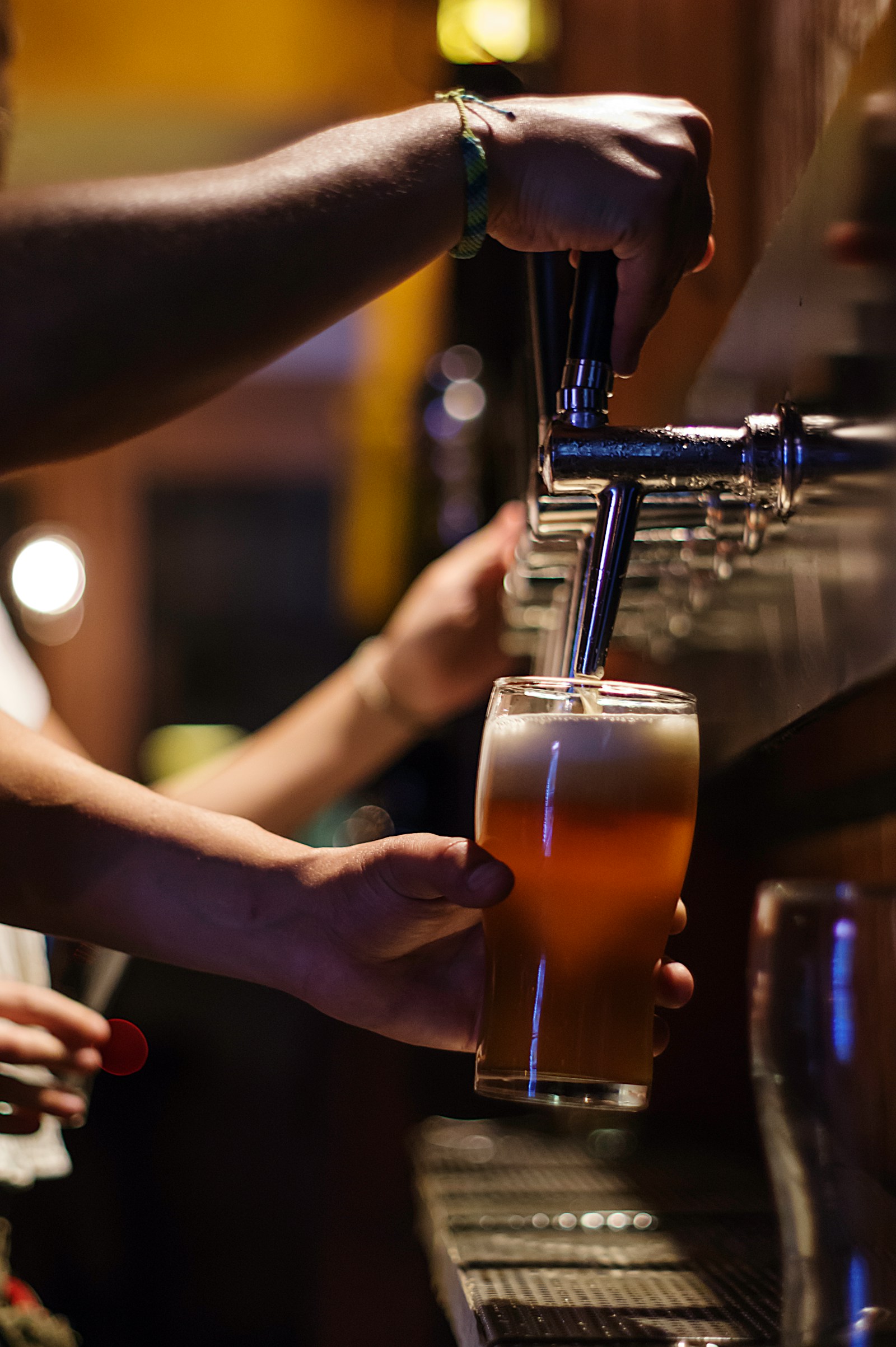 Nhân viên quầy bar đang gạt vòi rót bia vàng vào ly thủy tinh cao, bọt trắng dày trên mặt