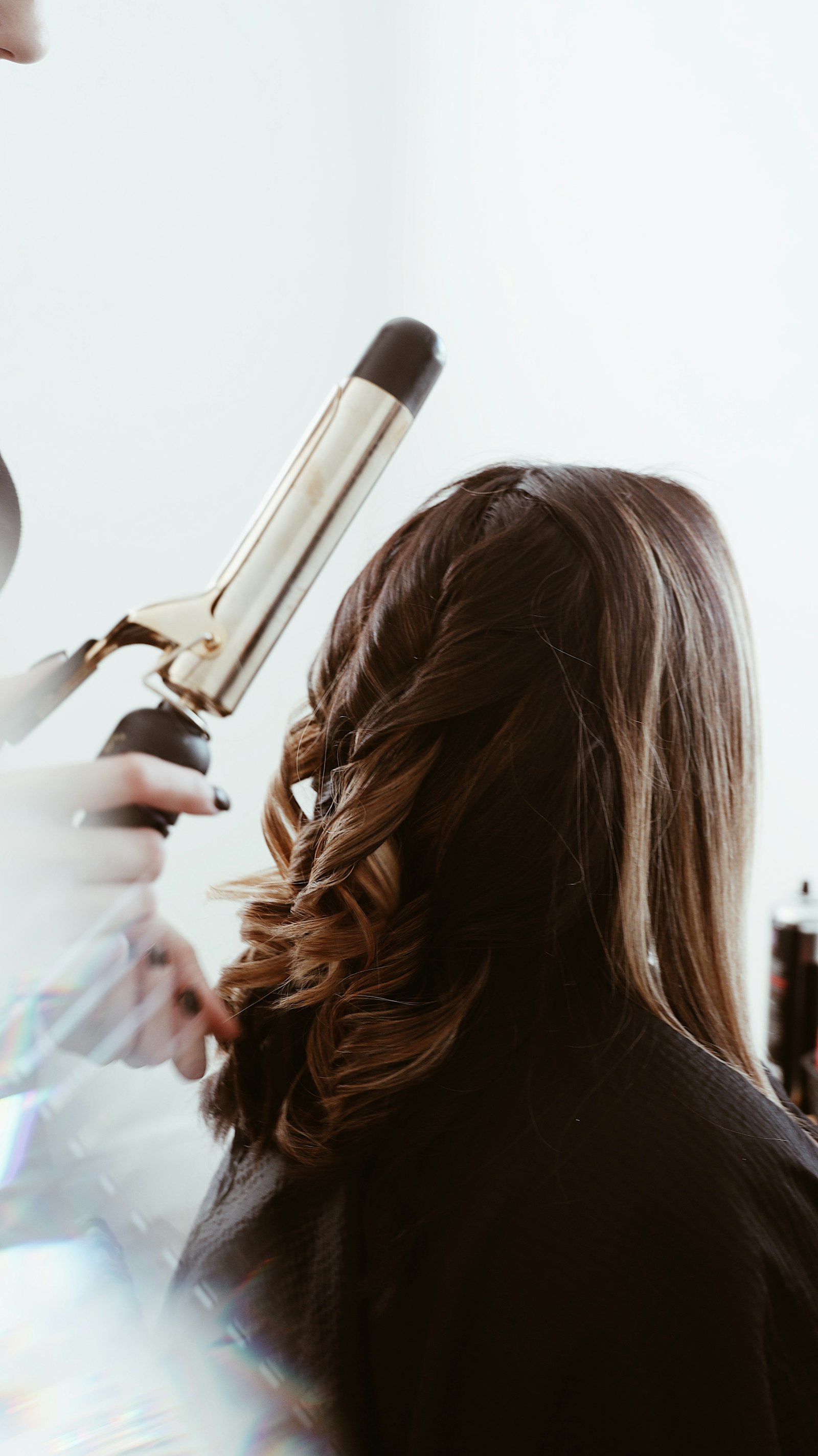 Thợ đang uốn tóc bằng máy uốn cho khách tóc dài tại salon