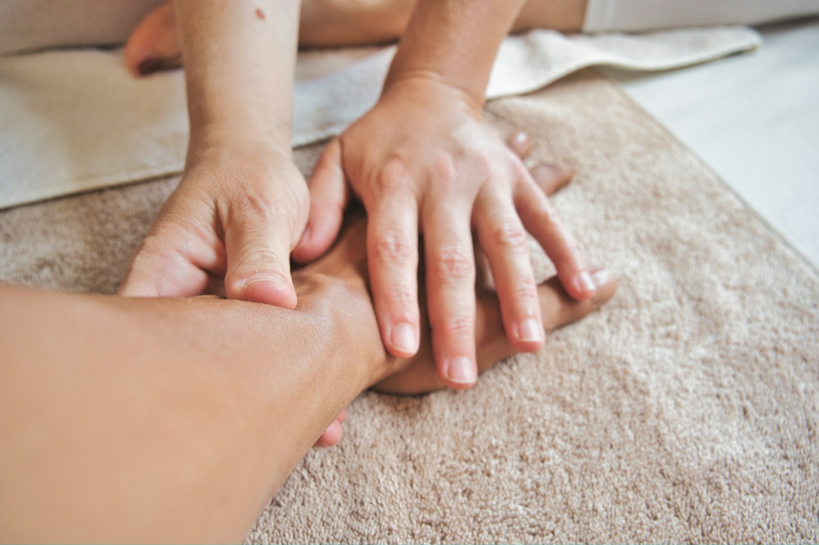 Đôi tay chuyên viên đang xoa bóp nhẹ vùng cẳng tay khách trên khăn bông
