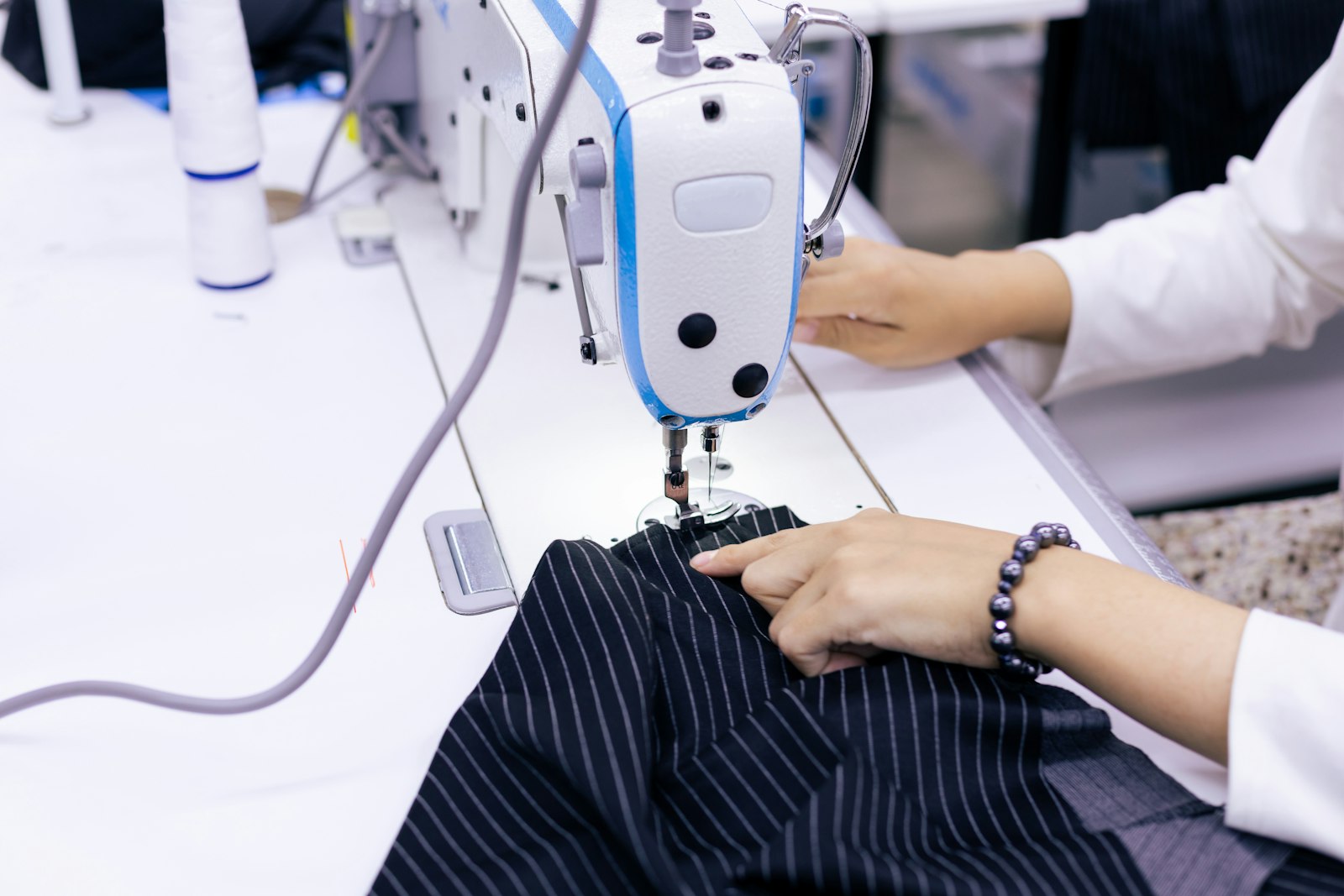 Đôi tay thợ may đưa mảnh vải kẻ sọc qua chân vịt máy may công nghiệp