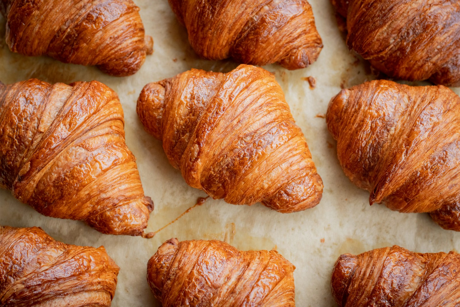 Chín chiếc croissant vừa ra lò xếp trên giấy nến, vỏ vàng nâu bóng và tách lớp rõ.