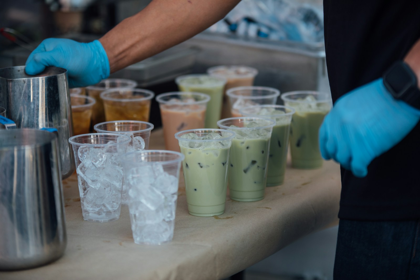 Nhân viên đeo găng tay xếp hàng loạt ly trà sữa matcha và trà sữa lên quầy chuẩn bị giao