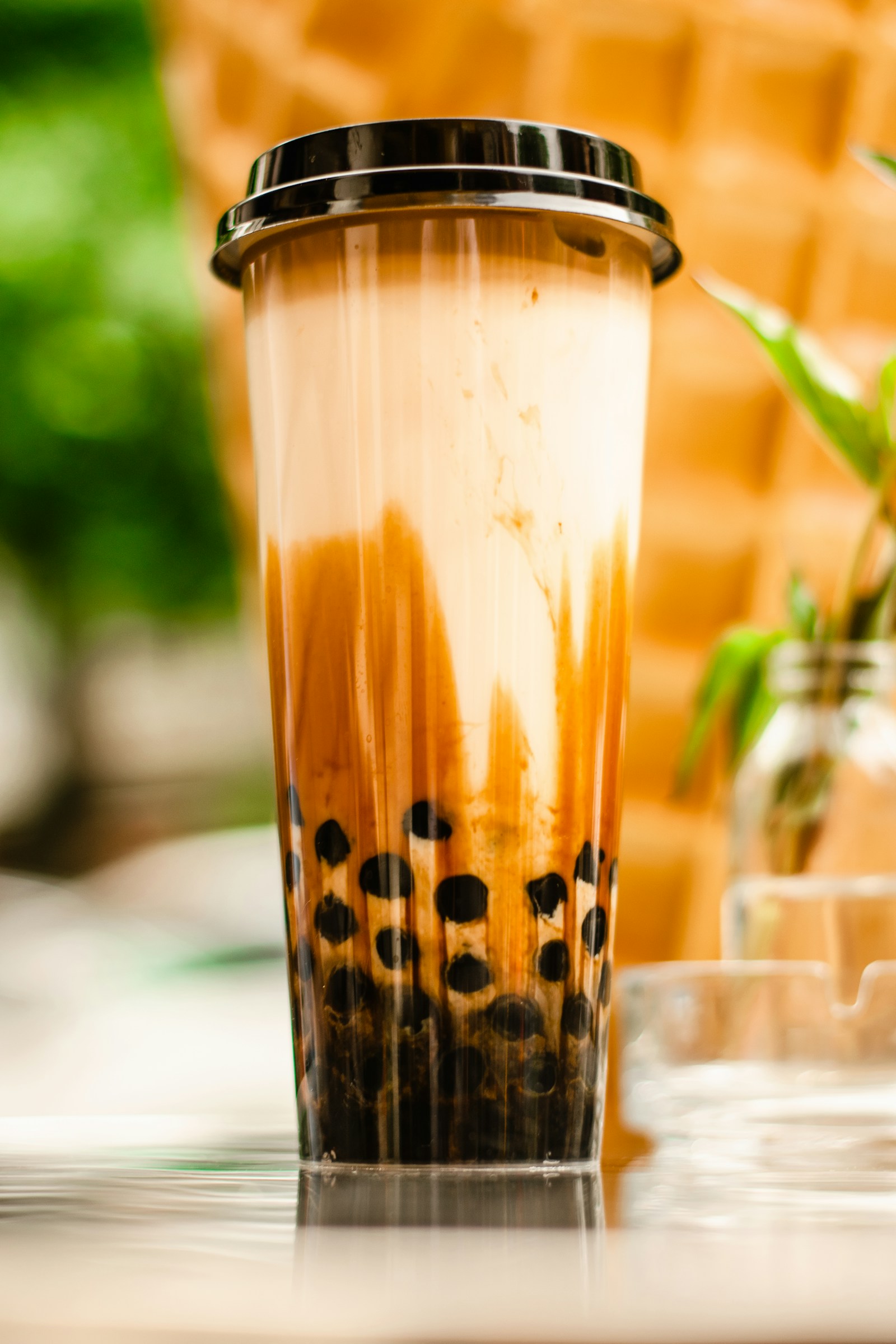 Ly trà sữa trân châu đường đen size L đậy nắp đen đặt trên mặt bàn kính