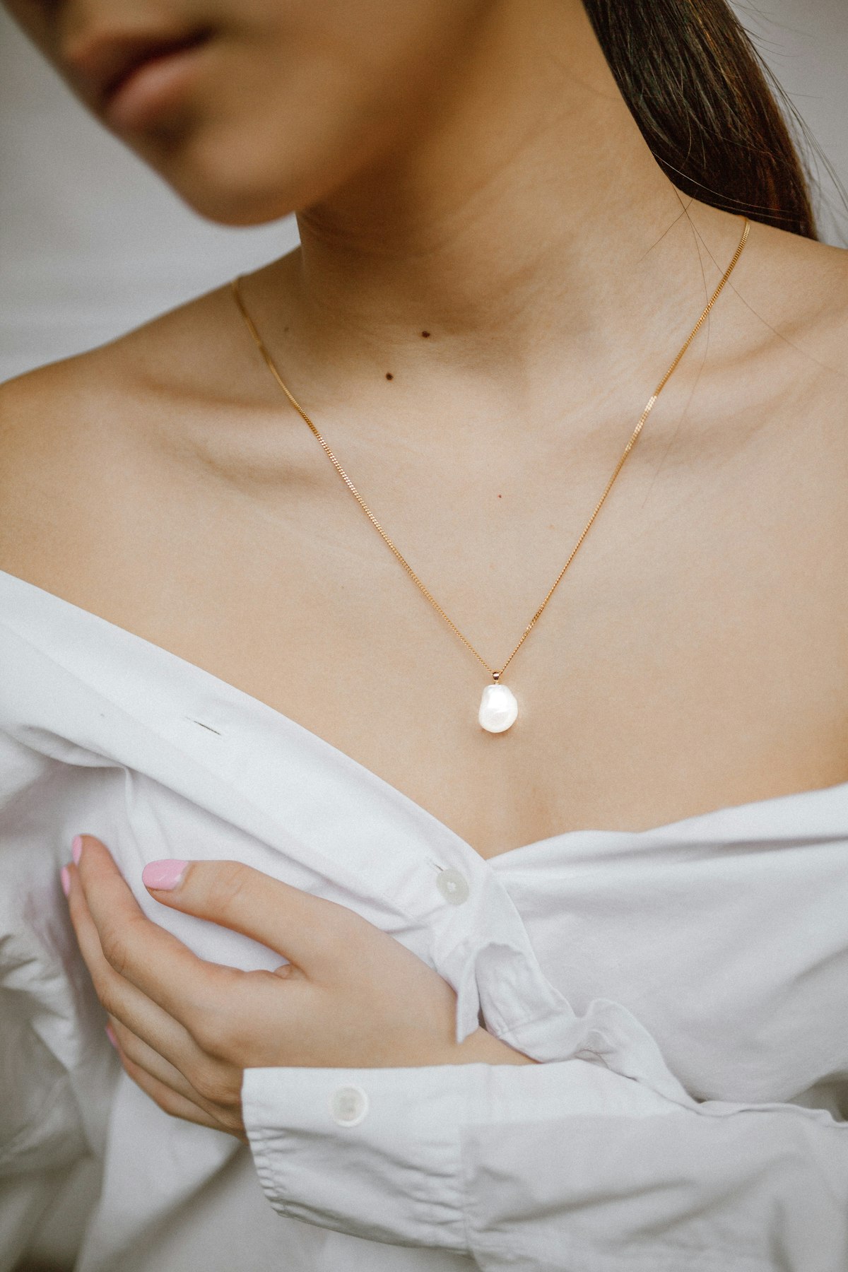 Cô gái mặc sơ mi trắng đeo dây chuyền bạc mảnh có mặt tròn nhỏ nằm giữa xương quai xanh